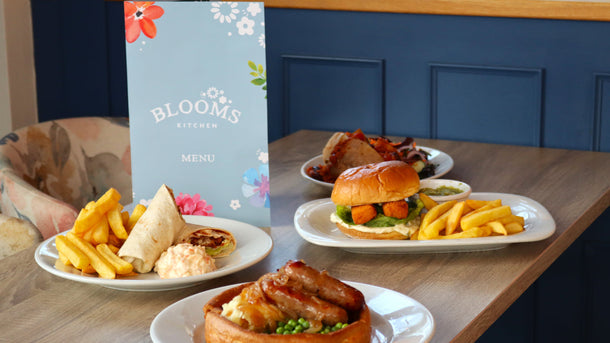 Plates of food on a table with a 'Blooms' menu in the background