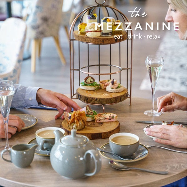 People enjoying afternoon tea with a three-tiered cake stand, teacups, and pastries on a wooden table.