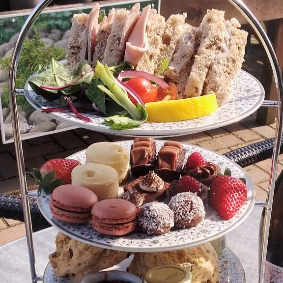 Three-tiered tray with sandwiches, pastries, and fruits on a outdoor setting