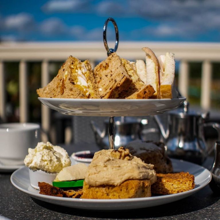 Two-tiered cake stand with assorted finger sandwiches and pastries outdoors.